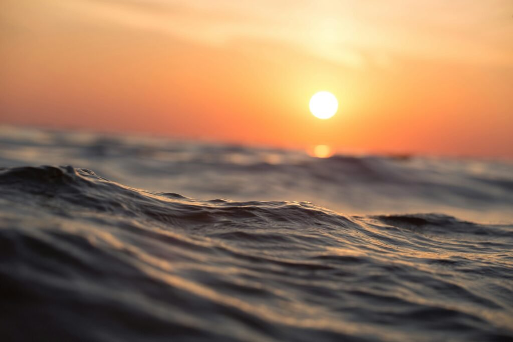 Imagem do mar com leves ondulações, iluminado pelo sol, próximo à linha do horizonte.